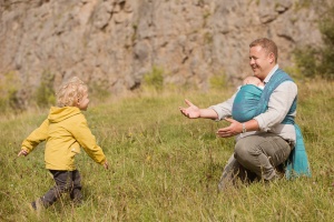 Warton Crag Lancashire - Dad with baby twin in a baby carrier holding out his atms while his toddler son runs towards him